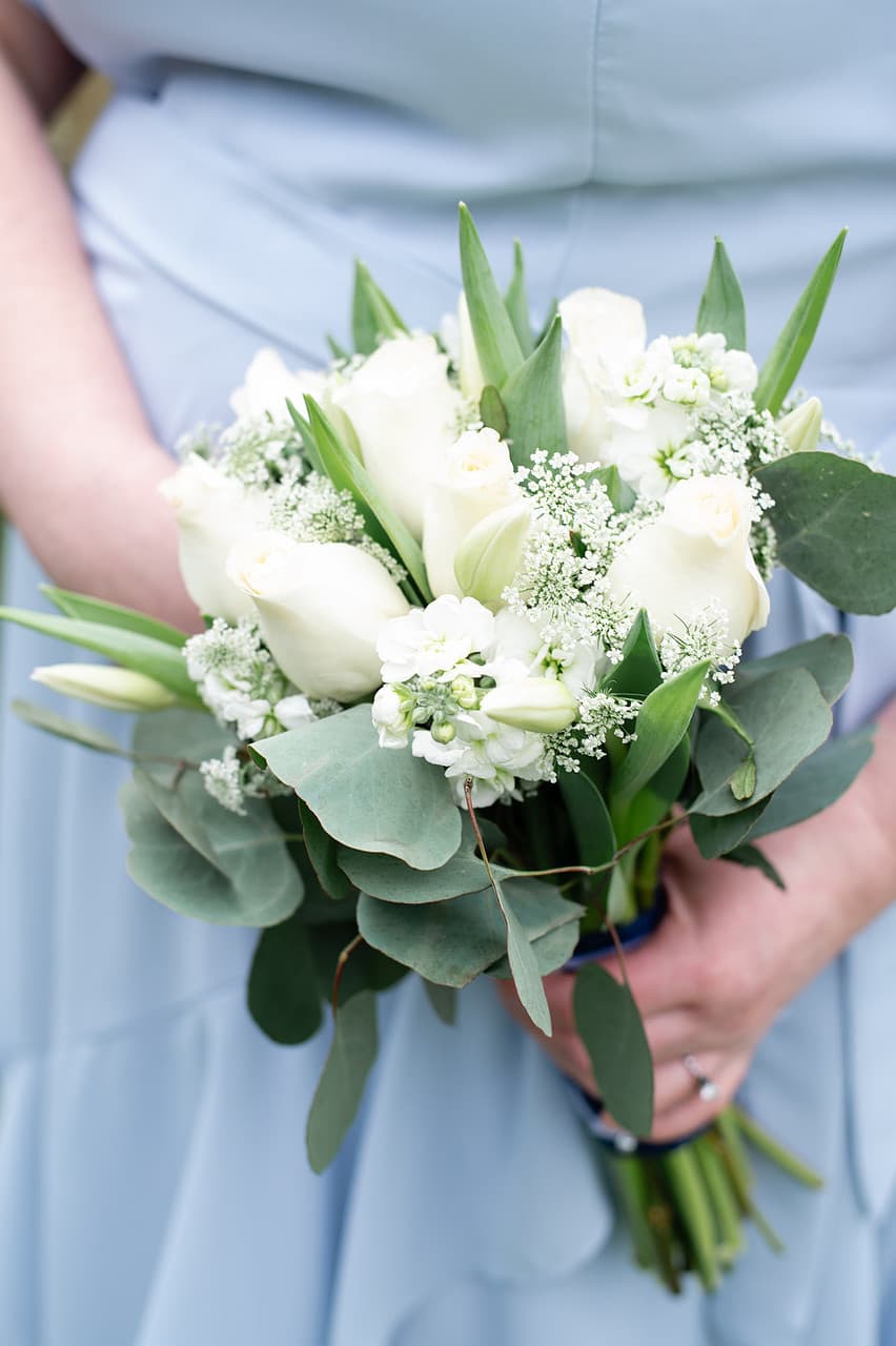 A person in a blue dress holds a bouquet of white roses and greenery.