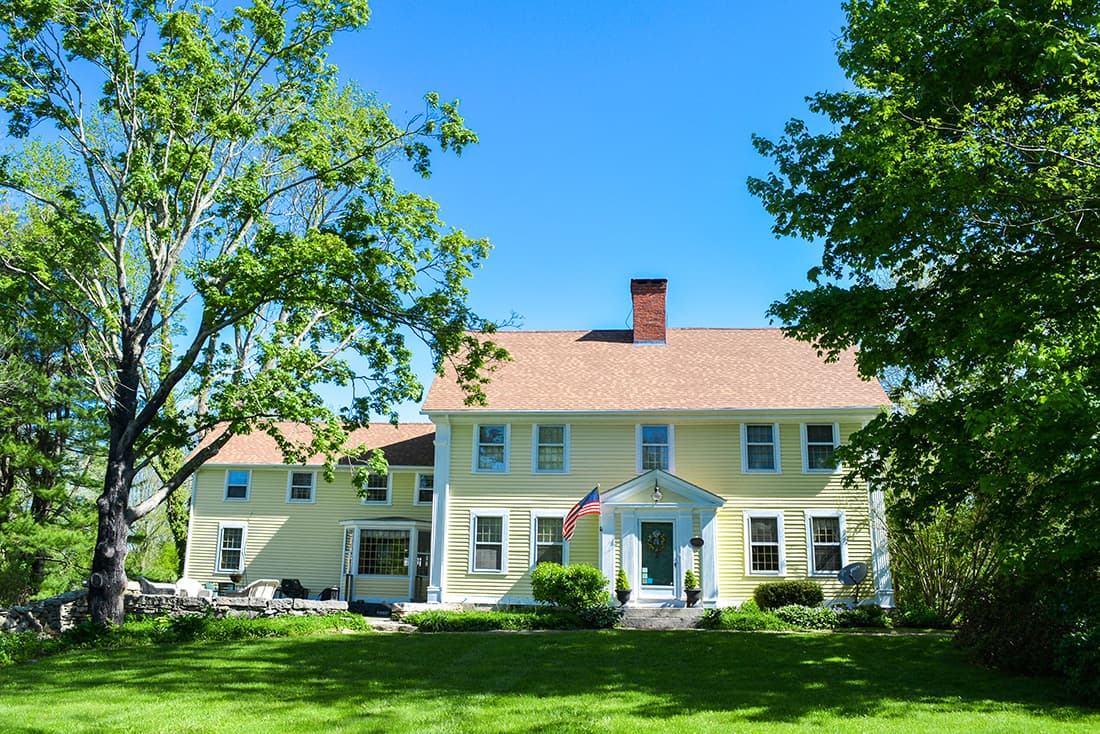 A large yellow house with a red roof surrounded by green trees and grass.