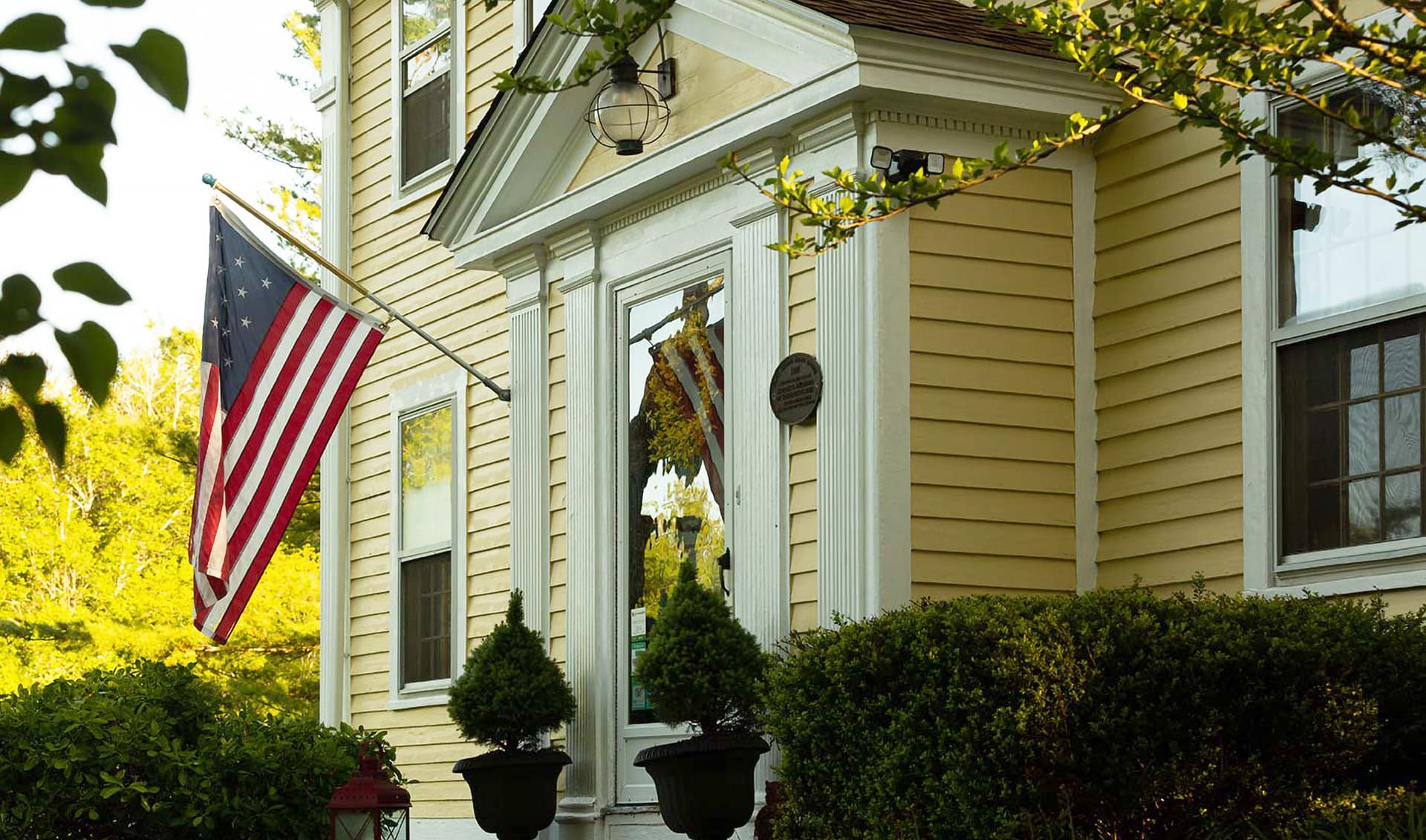 A yellow house with an American flag hanging from the porch.