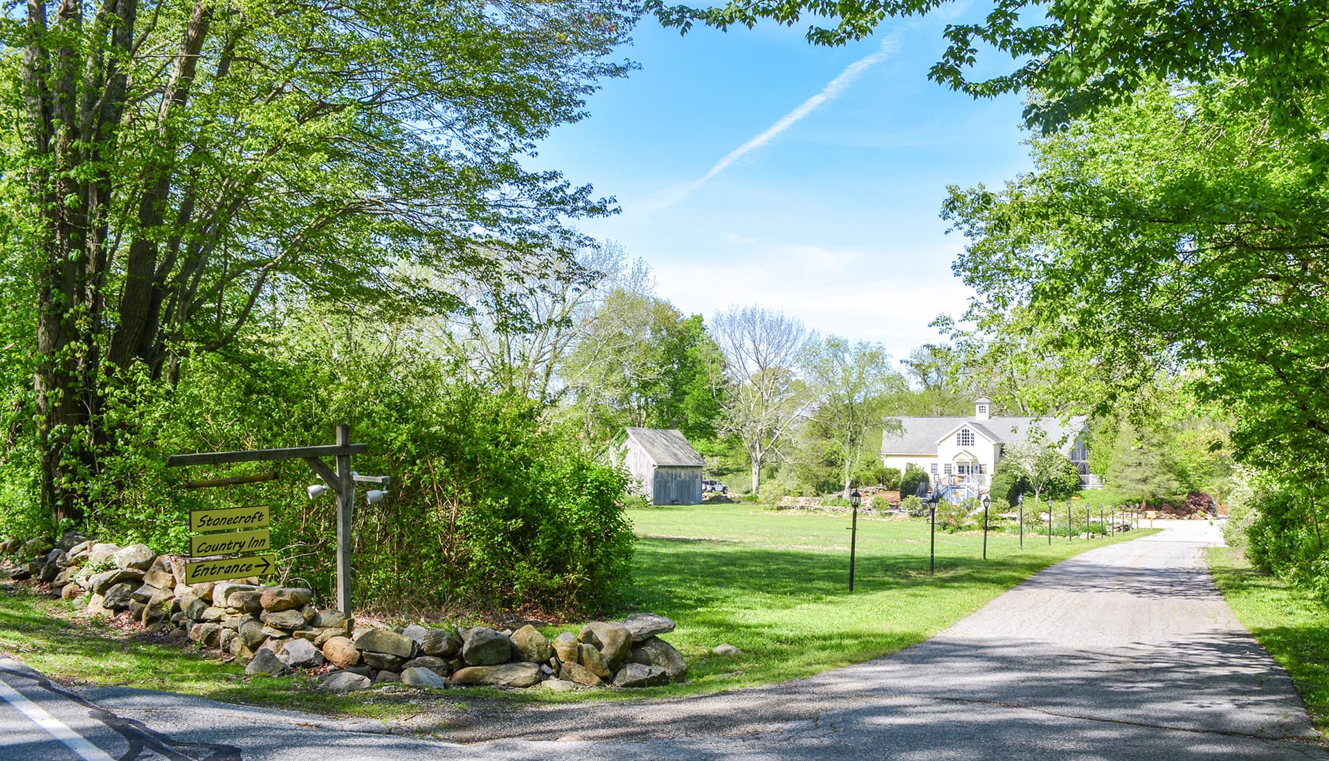 A scenic dirt road leading to a country house surrounded by greenery.