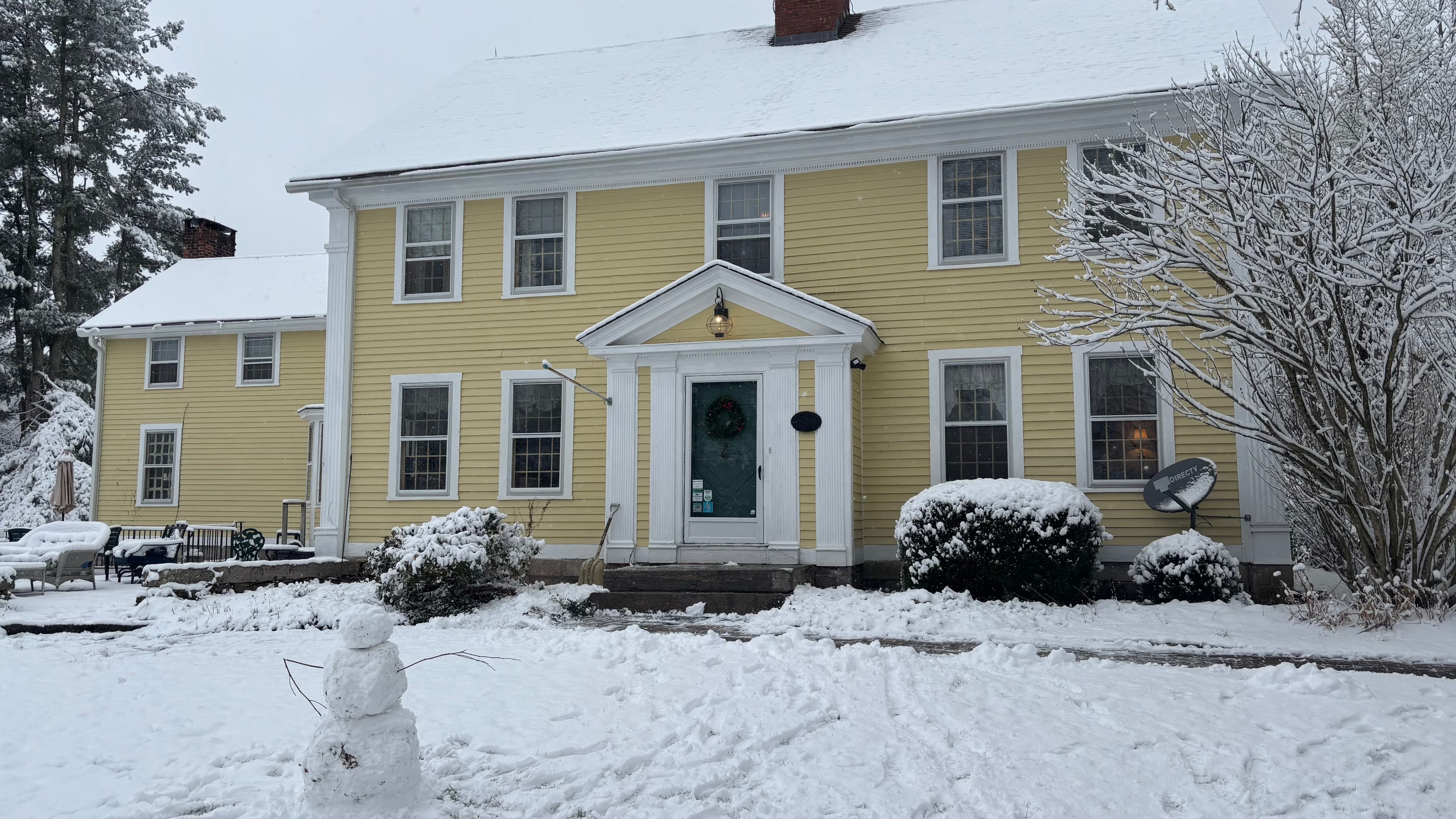 A yellow house with snow-covered grounds and a small snowman in the front yard. A yellow house with snow-covered grounds and a small snowman in the front yard.