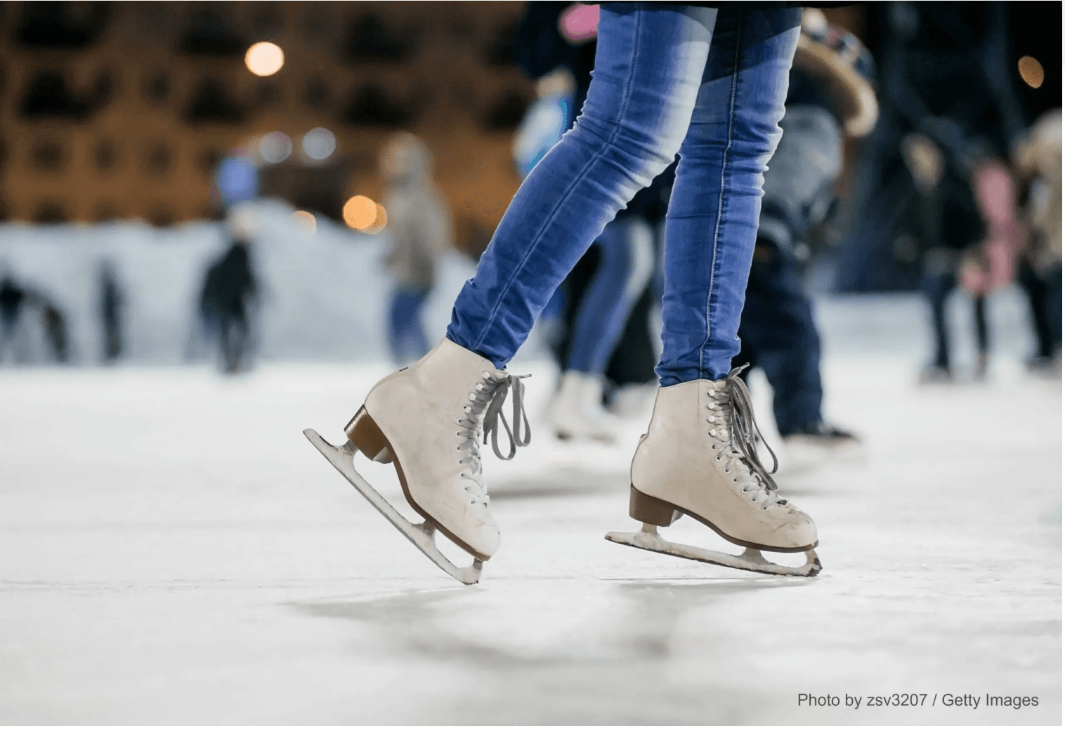 A pair of ice skates gliding on a rink with blurred figures in the background. A pair of ice skates gliding on a rink with blurred figures in the background.