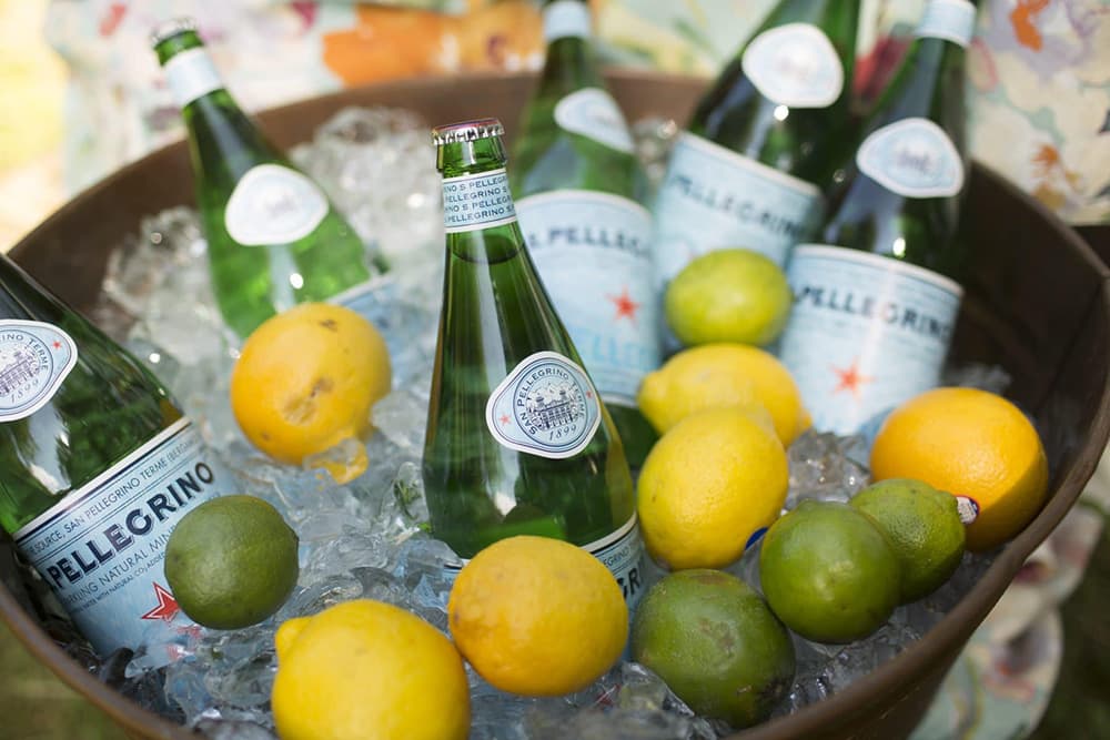 A metal bowl filled with ice, sparkling water bottles, and fresh lemons and limes.