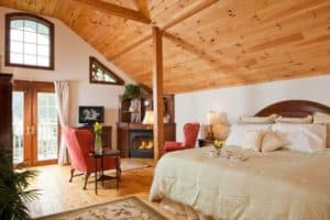 A cozy bedroom with a wooden ceiling, large windows, a fireplace, and elegant decor.