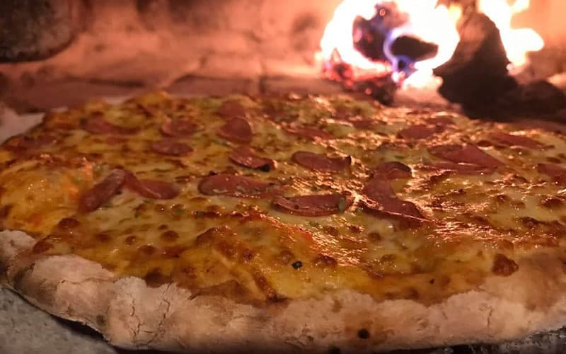 A freshly baked pizza with pepperoni is placed in front of a glowing wood-fired oven.