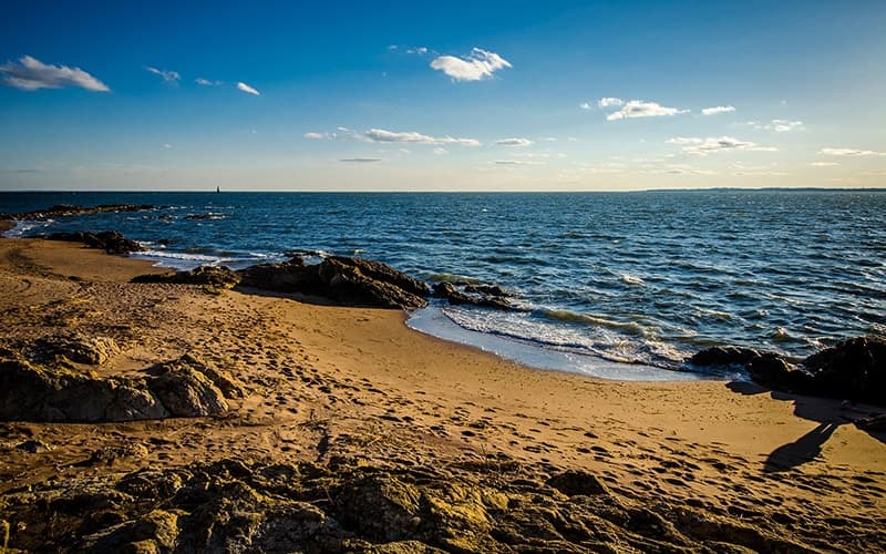 A scenic beach with rocky shorelines and gentle waves under a clear blue sky.