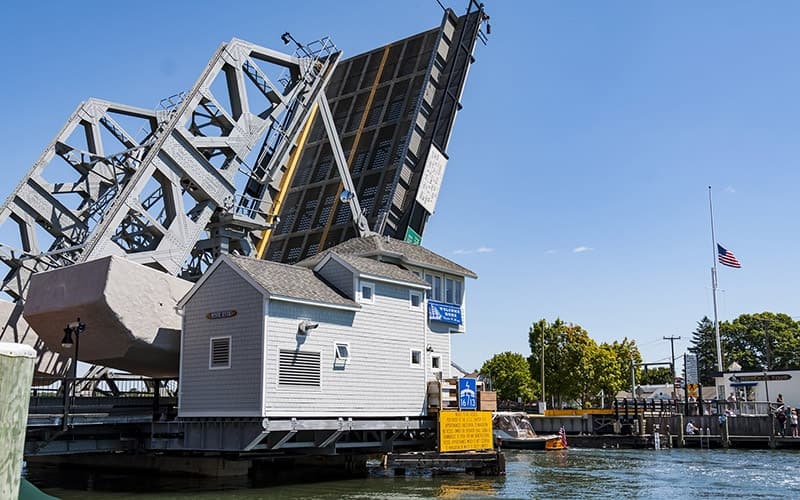 A drawbridge rises beside a small houseboat on a sunny day.