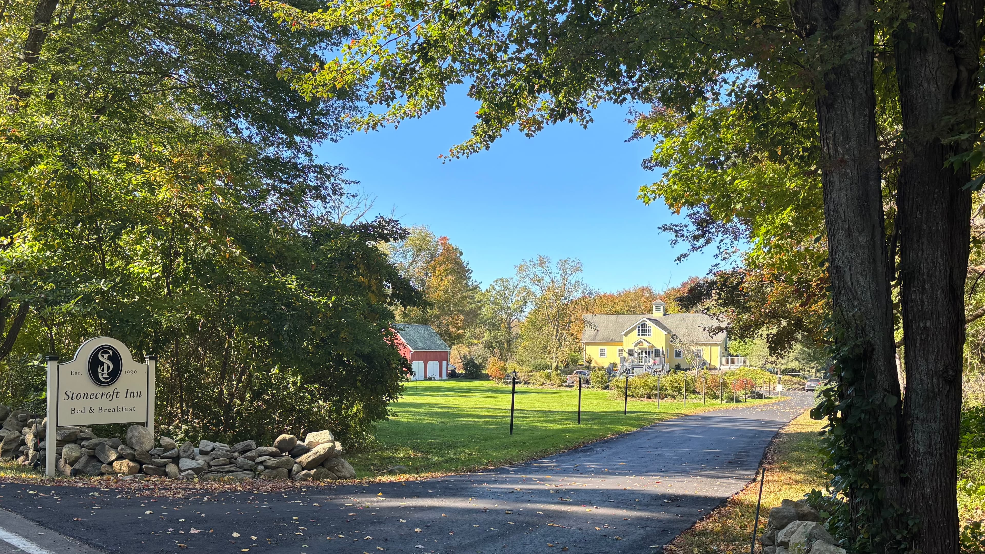 A serene view of the entrance to Stonecrop Inn, framed by trees and lined with a stone wall.