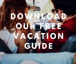 A couple sits in a car, looking at a map with the text "Download Our Free Vacation Guide" overlayed.