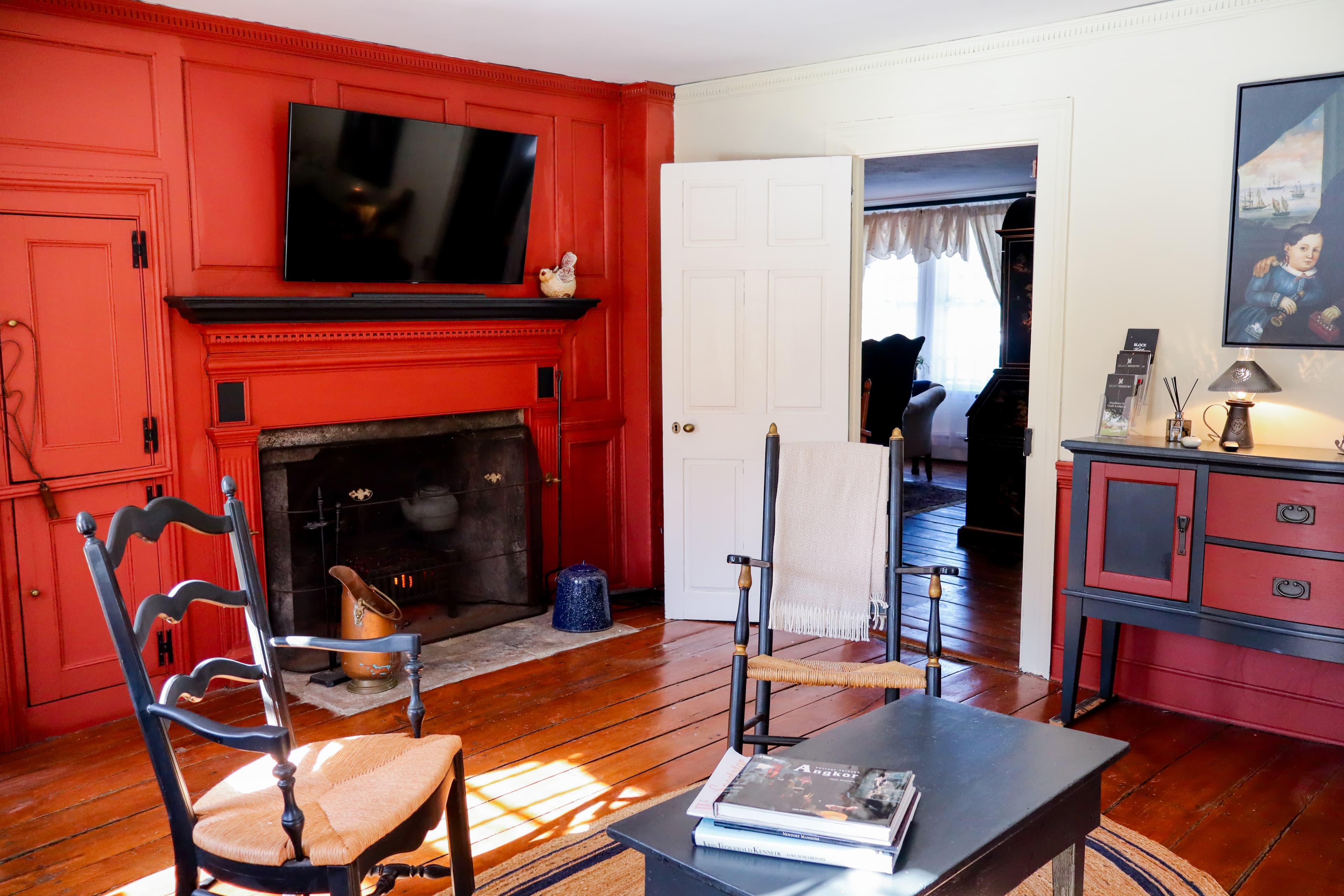 A cozy room featuring red walls, a television above a fireplace, and a mix of vintage and modern furniture.