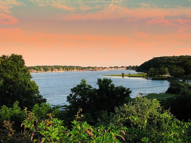A serene view of a river bordered by lush greenery and a colorful sky.