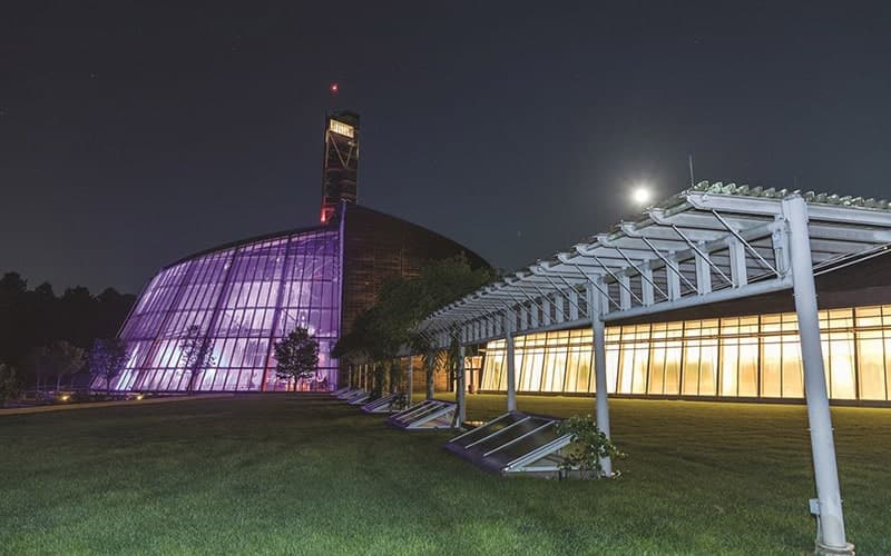A modern glass building illuminated in purple under a night sky with a visible moon.